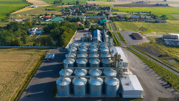 Aerial view of large grain bins surrounded by agricultural fields and rural buildings in Poland.