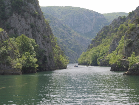 View of Matka Canyon with steep rocky cliffs lush green vegetation and small boats on the calm river in Matka Grad Skopje North Macedonia.
