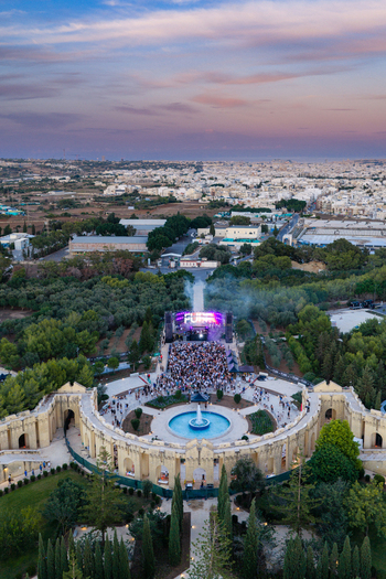 Attard Malta 20 September 2026 Aerial view of Ta Qali National Park featuring an outdoor concert stage with a large crowd a central fountain and lush greenery under a sunset sky. Attard Malta 20 September 2026 Aerial view of Ta Qali National Park featuring an outdoor concert stage with a large crowd a central fountain and lush greenery under a sunset sky.
