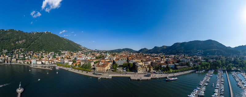 Aerial view of the historic city of Como nestled between mountains and Lake Como featuring a harbor with boats terracotta rooftops and the cathedral dome in Como Lombardy Italy.