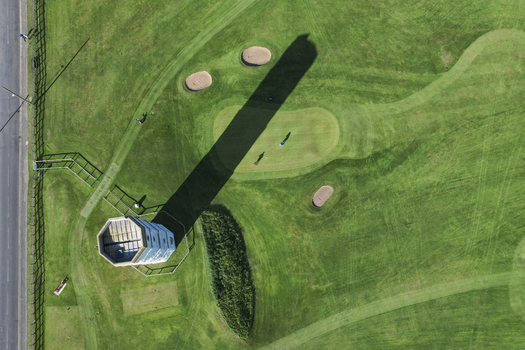 Aerial view of the Old Flamborough Lighthouse casting a long shadow over the surrounding green golf course with sand bunkers and a nearby road in Bridlington England United Kingdom. Aerial view of the Old Flamborough Lighthouse casting a long shadow over the surrounding green golf course with sand bunkers and a nearby road in Bridlington England United Kingdom.