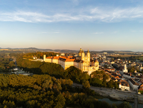 Aerial view of Melk Abbey perched on a rocky outcrop overlooking the town of Melk surrounded by lush trees and golden hour light in Melk Niederosterreich Austria. Aerial view of Melk Abbey perched on a rocky outcrop overlooking the town of Melk surrounded by lush trees and golden hour light in Melk Niederosterreich Austria.