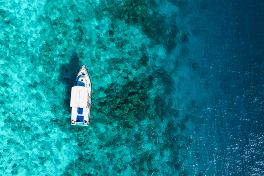 Aerial view of a white boat floating on clear turquoise water over a coral reef in Vashafaru Haa Alif Atoll Maldives. Aerial view of a white boat floating on clear turquoise water over a coral reef in Vashafaru Haa Alif Atoll Maldives.