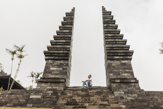 View of Cetho Temple with a man sitting on the stone steps between the iconic split gates under an overcast sky Kecamatan Jenawi Jawa Tengah Indonesia. View of Cetho Temple with a man sitting on the stone steps between the iconic split gates under an overcast sky Kecamatan Jenawi Jawa Tengah Indonesia.