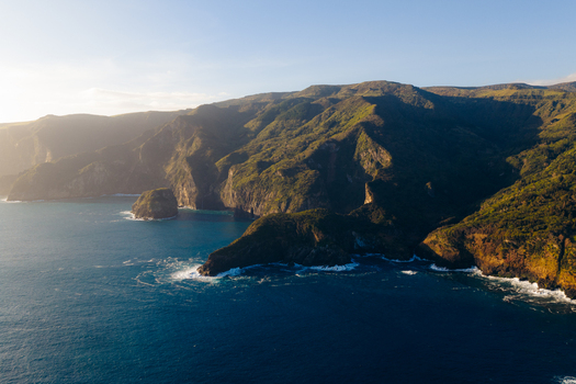 Aerial view of the rugged coastline featuring steep green cliffs and deep blue ocean waters under warm golden sunlight in Ponta Delgada Acores Portugal. Aerial view of the rugged coastline featuring steep green cliffs and deep blue ocean waters under warm golden sunlight in Ponta Delgada Acores Portugal.