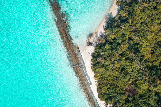 Aerial view of a lush tropical island with tall palm trees and dense vegetation surrounded by crystal clear turquoise lagoon water Innafinolhu Haa Alif Atoll Maldives. Aerial view of a lush tropical island with tall palm trees and dense vegetation surrounded by crystal clear turquoise lagoon water Innafinolhu Haa Alif Atoll Maldives.