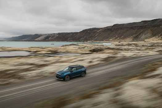 Aerial view of a blue SUV driving along a dirt road through the mossy volcanic landscape near Hlidarvatn in Sveitarfelagid Olfus Iceland. Aerial view of a blue SUV driving along a dirt road through the mossy volcanic landscape near Hlidarvatn in Sveitarfelagid Olfus Iceland.