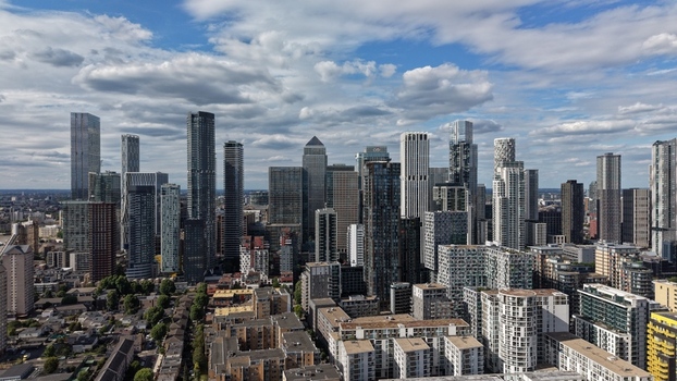 London United Kingdom 16 June 2026 Aerial view of Canary Wharf skyline featuring modern skyscrapers glass facades and residential buildings under a cloudy blue sky.