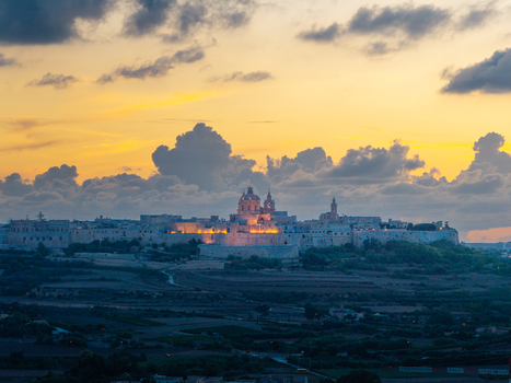 Aerial view of the historic fortified city of Mdina illuminated by golden hour light featuring its cathedral dome and stone walls surrounded by rural landscape in Mdina Western Region Malta.