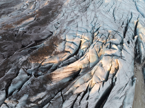 Aerial view of Svinafellsjokull glacier featuring deep blue crevasses and dark volcanic ash deposits in Sveitarfelagid Hornafjordur Iceland. Aerial view of Svinafellsjokull glacier featuring deep blue crevasses and dark volcanic ash deposits in Sveitarfelagid Hornafjordur Iceland.
