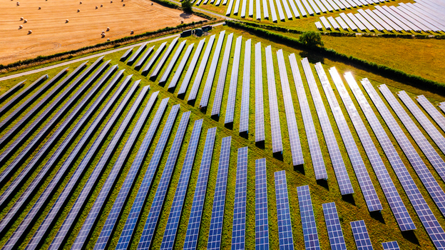 Aerial view of a large solar farm with rows of photovoltaic panels set in green fields next to a harvested field with hay bales in Dorset England United Kingdom. Aerial view of a large solar farm with rows of photovoltaic panels set in green fields next to a harvested field with hay bales in Dorset England United Kingdom.