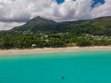 Aerial view of turquoise waters meet the sandy shore lush greenery climbs towards the mountainous backdrop creating a vibrant contrast Victoria Seychelles. Aerial view of turquoise waters meet the sandy shore lush greenery climbs towards the mountainous backdrop creating a vibrant contrast Victoria Seychelles.