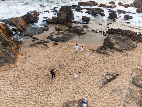 Aerial view of a couple walking on a sandy beach surrounded by large rocks and crashing waves during golden hour in Galle Southern Province Sri Lanka. Aerial view of a couple walking on a sandy beach surrounded by large rocks and crashing waves during golden hour in Galle Southern Province Sri Lanka.