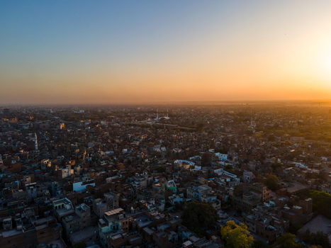 Aerial view of Minar e Pakistan rising above the dense urban landscape of Lahore at sunset with warm golden light illuminating the rooftops and streets of Lahore Punjab Pakistan.