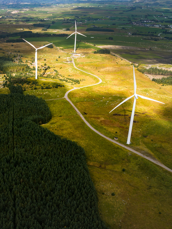 Aerial view of Hog Jaeren vindkraftverk wind turbines set in a rolling green landscape with a winding road and dense forest in Ha Municipality Rogaland Norway.