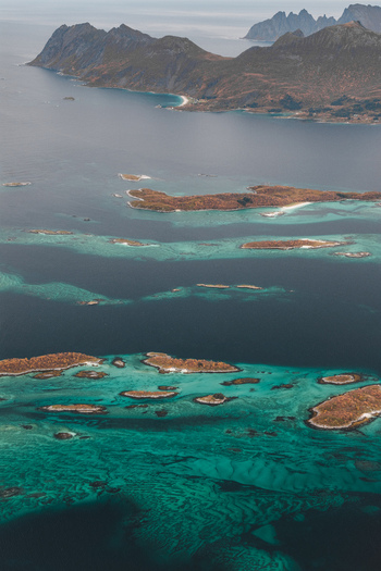 Aerial view of the rugged coastline and turquoise waters of Senja featuring numerous small islands rocky terrain and clear sea in Senja Troms Norway.