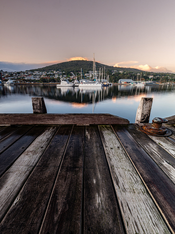 View of Princess Royal Harbour with boats moored in the calm water reflecting the soft light of dawn seen from a weathered wooden pier in Albany WA Australia. View of Princess Royal Harbour with boats moored in the calm water reflecting the soft light of dawn seen from a weathered wooden pier in Albany WA Australia.