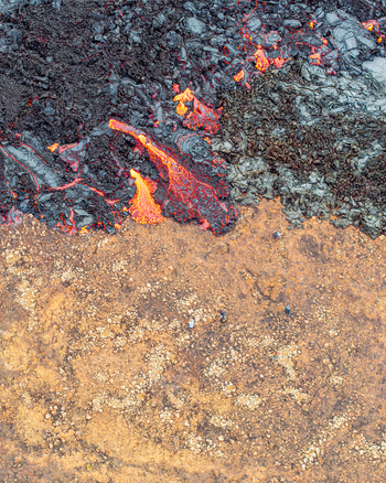 Aerial view of glowing molten lava flowing over dark volcanic rock next to a barren landscape with people walking nearby in Iceland. Aerial view of glowing molten lava flowing over dark volcanic rock next to a barren landscape with people walking nearby in Iceland.