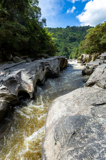 View of the Estrecho del Rio Magdalena with rushing water flowing through narrow eroded rock formations surrounded by lush green hills in San Agustin Huila Colombia.