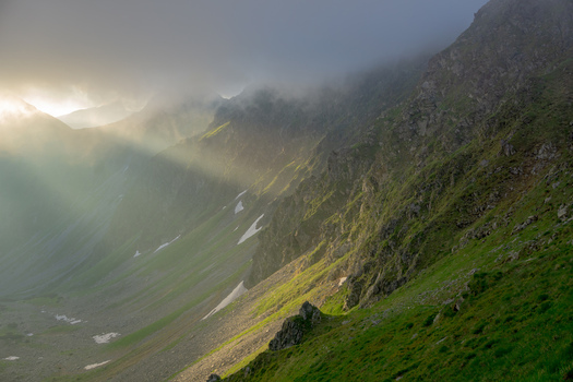 View of Smutne sedlo in Western Tatras with dramatic sunbeams piercing through thick fog over steep green slopes and rocky ridges in Ziar Zilina Region Slovakia. View of Smutne sedlo in Western Tatras with dramatic sunbeams piercing through thick fog over steep green slopes and rocky ridges in Ziar Zilina Region Slovakia.
