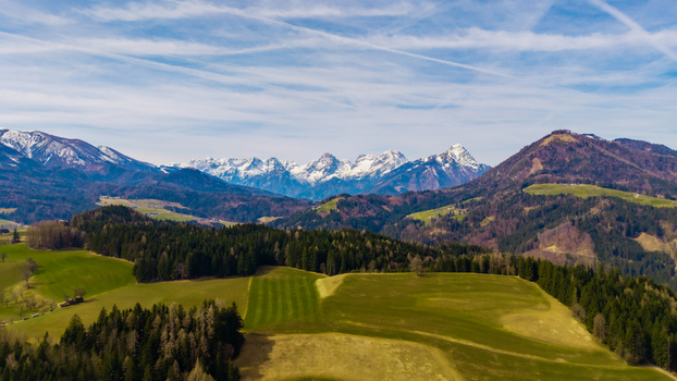Aerial view of verdant fields nestled amongst the foothills contrasted by the majestic snow capped Alps under a clear sky Windischgarsten Upper Austria Austria. Aerial view of verdant fields nestled amongst the foothills contrasted by the majestic snow capped Alps under a clear sky Windischgarsten Upper Austria Austria.