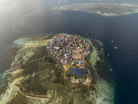 Aerial view of the densely populated village on Pulau Mesa surrounded by shallow turquoise waters coral reefs and small boats in Kecamatan Komodo Nusa Tenggara Timur Indonesia. Aerial view of the densely populated village on Pulau Mesa surrounded by shallow turquoise waters coral reefs and small boats in Kecamatan Komodo Nusa Tenggara Timur Indonesia.