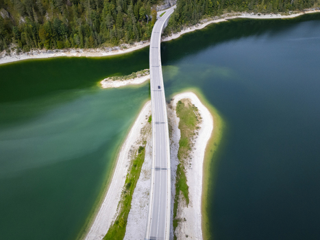 Aerial view of a bridge cutting through the contrasting turquoise and dark blue waters of Sylvensteinsee surrounded by lush green forests Sylvensteinspeicher Bayern Germany. Aerial view of a bridge cutting through the contrasting turquoise and dark blue waters of Sylvensteinsee surrounded by lush green forests Sylvensteinspeicher Bayern Germany.
