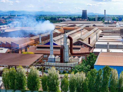 Aerial view of the industrial plant with smoking chimneys cooling towers and large warehouses under a blue sky with mountains in the distance in Dalmine Lombardy Italy. Aerial view of the industrial plant with smoking chimneys cooling towers and large warehouses under a blue sky with mountains in the distance in Dalmine Lombardy Italy.