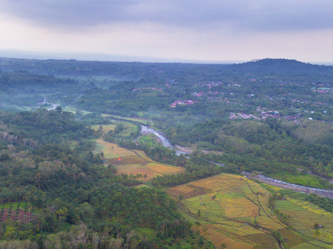 Aerial view of Taba Tembilang featuring a winding river through lush hills terraced rice fields and tropical vegetation under an overcast sky in Arga Makmur Bengkulu Indonesia.
