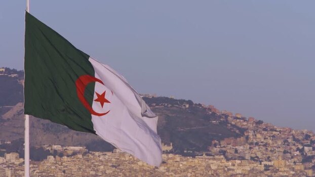 Aerial view of Algerian flag waving over hillside city Algeria.