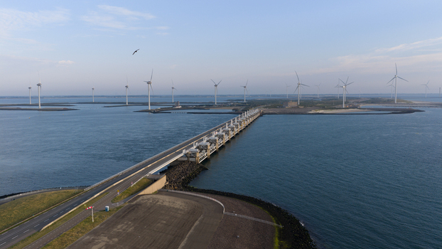 Aerial view of the Eastern Scheldt Storm Surge Barrier stretching across the water with wind turbines in the background in Vrouwenpolder Zeeland Netherlands. Aerial view of the Eastern Scheldt Storm Surge Barrier stretching across the water with wind turbines in the background in Vrouwenpolder Zeeland Netherlands.