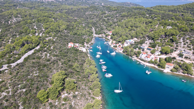 Aerial view of the turquoise waters of a narrow bay with anchored sailboats and yachts surrounded by lush pine forests and coastal houses in Necujam Split Dalmatia County Croatia. Aerial view of the turquoise waters of a narrow bay with anchored sailboats and yachts surrounded by lush pine forests and coastal houses in Necujam Split Dalmatia County Croatia.