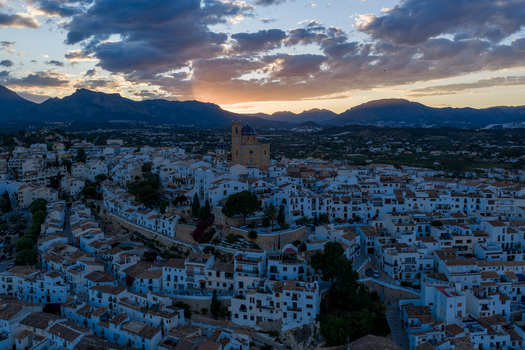 Aerial view of the historic white washed town of Altea with its iconic blue domed church nestled against the mountains under a dramatic sunset sky in Altea Valencian Community Spain.