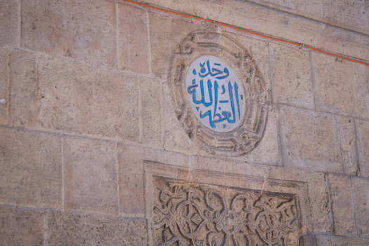 View of intricate blue Arabic calligraphy within a circular medallion on the historic stone walls of Al Azhar Mosque Cairo Egypt. View of intricate blue Arabic calligraphy within a circular medallion on the historic stone walls of Al Azhar Mosque Cairo Egypt.