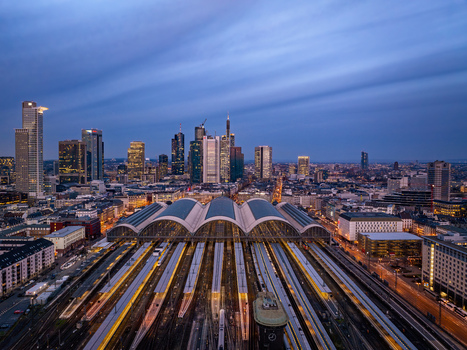 Aerial view of Hauptbahnhof s grand arches and tracks converging with the glowing modern city skyline at twilight Frankfurt am Main Hessen Germany.