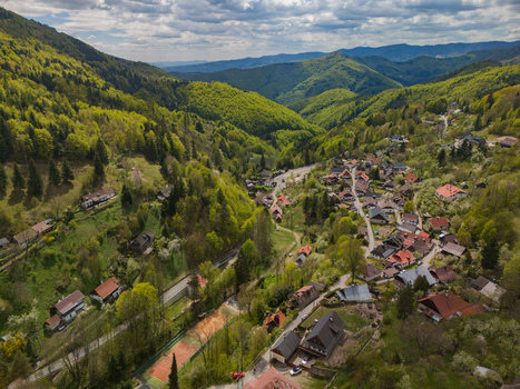 Aerial view of the historic village of Spania Dolina nestled in a lush green valley surrounded by forested hills under a cloudy sky in Spania Dolina Banska Bystrica Region Slovakia.