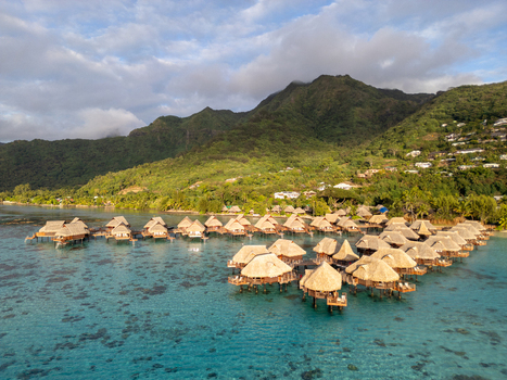 Aerial view of Sofitel Kia Ora Moorea Beach Resort with overwater bungalows in a turquoise lagoon against lush green mountains in Moorea Maiao Windward Islands French Polynesia. Aerial view of Sofitel Kia Ora Moorea Beach Resort with overwater bungalows in a turquoise lagoon against lush green mountains in Moorea Maiao Windward Islands French Polynesia.