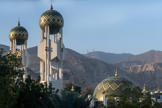 View of the Mohammed Al Ameen Mosque with its distinctive patterned domes and minarets set against a backdrop of rugged mountains in Muscat Muscat Governorate Oman. View of the Mohammed Al Ameen Mosque with its distinctive patterned domes and minarets set against a backdrop of rugged mountains in Muscat Muscat Governorate Oman.