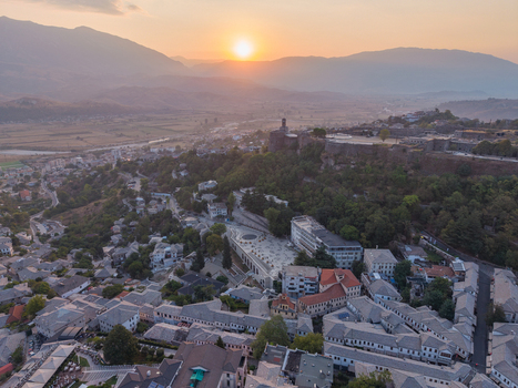 Aerial view of Gjirokaster Castle overlooking the historic stone city rooftops during a golden sunset in Gjirokaster Gjirokaster County Albania. Aerial view of Gjirokaster Castle overlooking the historic stone city rooftops during a golden sunset in Gjirokaster Gjirokaster County Albania.