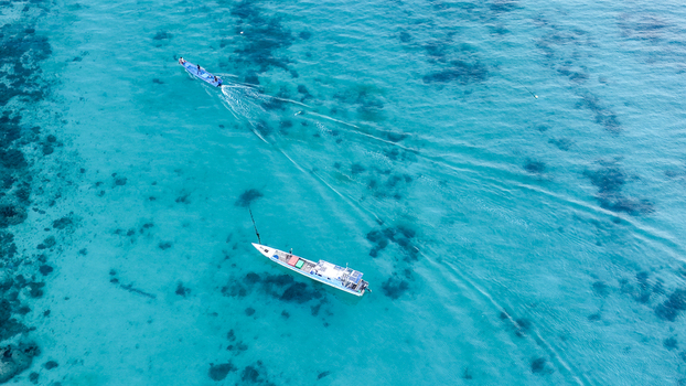 Aerial view of two traditional wooden boats navigating through the clear turquoise waters of the coral reefs surrounding Pulau Derawan East Kalimantan Indonesia.