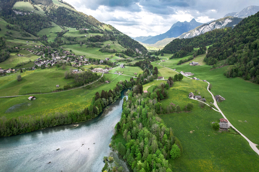 Aerial view of Lac du Vernex surrounded by the village of Rossiniere lush green meadows and the Swiss Alps under a cloudy sky Rossiniere Vaud Switzerland.