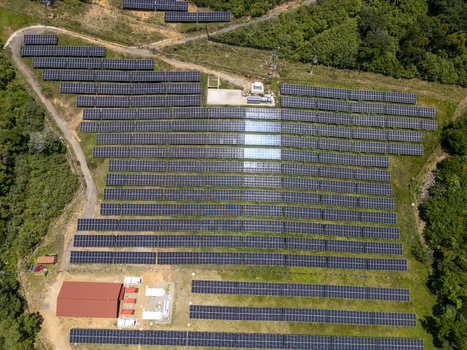 Aerial view of a large solar panel farm nestled on a lush green hillside surrounded by tropical forest in Guanaja Bay Islands Department Honduras.