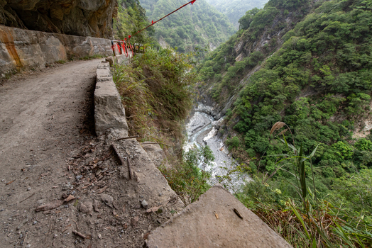 View of the narrow cliffside trail in Taroko National Park with a stone wall barrier overlooking a deep gorge and river in Xiulin Township Hualien County Taiwan.