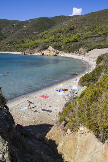 View of turquoise waters meet the sandy beach framed by rugged cliffs and lush green hills under a clear blue sky in Lacona Elba Italy. View of turquoise waters meet the sandy beach framed by rugged cliffs and lush green hills under a clear blue sky in Lacona Elba Italy.