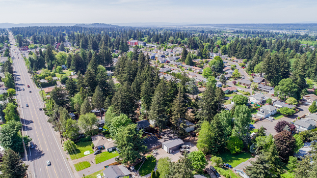 Aerial view of Northeast Glisan Street running through a lush suburban neighborhood with dense evergreen trees and residential houses under a clear blue sky in Portland Oregon United States. Aerial view of Northeast Glisan Street running through a lush suburban neighborhood with dense evergreen trees and residential houses under a clear blue sky in Portland Oregon United States.