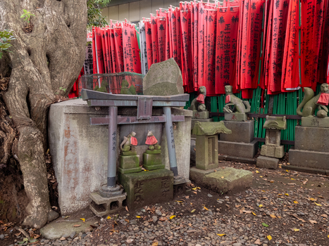 View of weathered stone foxes and miniature torii gates stand beneath vibrant red banners in a Japanese shrine Narita Chiba Japan. View of weathered stone foxes and miniature torii gates stand beneath vibrant red banners in a Japanese shrine Narita Chiba Japan.