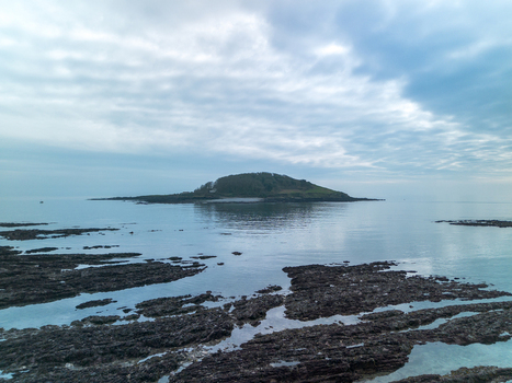 Aerial view of Looe Island surrounded by the sea with rocky formations in the foreground under a cloudy sky in Looe Cornwall United Kingdom. Aerial view of Looe Island surrounded by the sea with rocky formations in the foreground under a cloudy sky in Looe Cornwall United Kingdom.