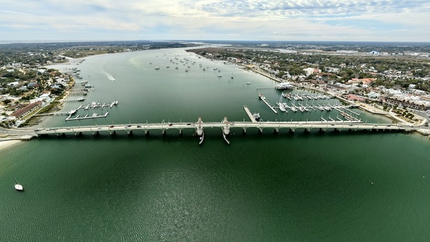 Aerial view of the Bridge of Lions spanning the Matanzas River with marinas docked boats and the historic city skyline under a bright sky in St. Augustine Florida United States.