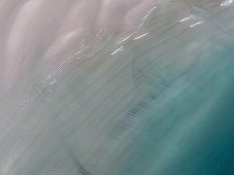 Aerial view of Gruinard Bay with gentle turquoise waves washing over the sandy shore and rippled textures under the clear water in Gruinard Scotland United Kingdom. Aerial view of Gruinard Bay with gentle turquoise waves washing over the sandy shore and rippled textures under the clear water in Gruinard Scotland United Kingdom.