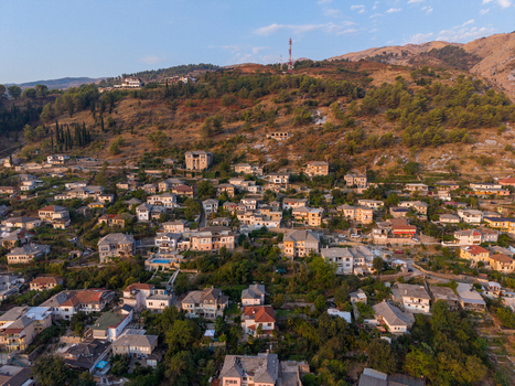 Aerial view of the historic city of Gjirokaster featuring traditional stone houses with slate roofs nestled on a hillside in Gjirokaster Gjirokaster County Albania. Aerial view of the historic city of Gjirokaster featuring traditional stone houses with slate roofs nestled on a hillside in Gjirokaster Gjirokaster County Albania.